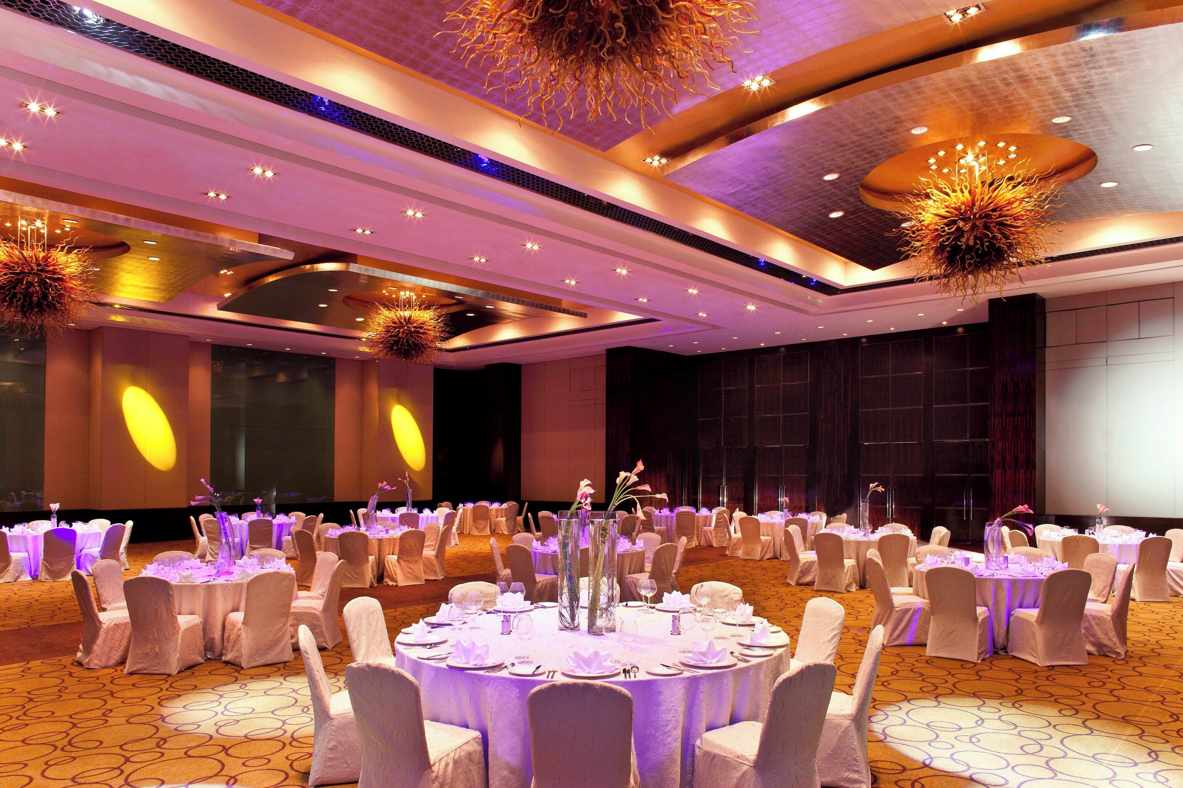 A banquet hall with round tables, white chairs, and a central floral arrangement.