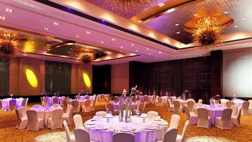 A banquet hall with round tables, white chairs, and a central floral arrangement.