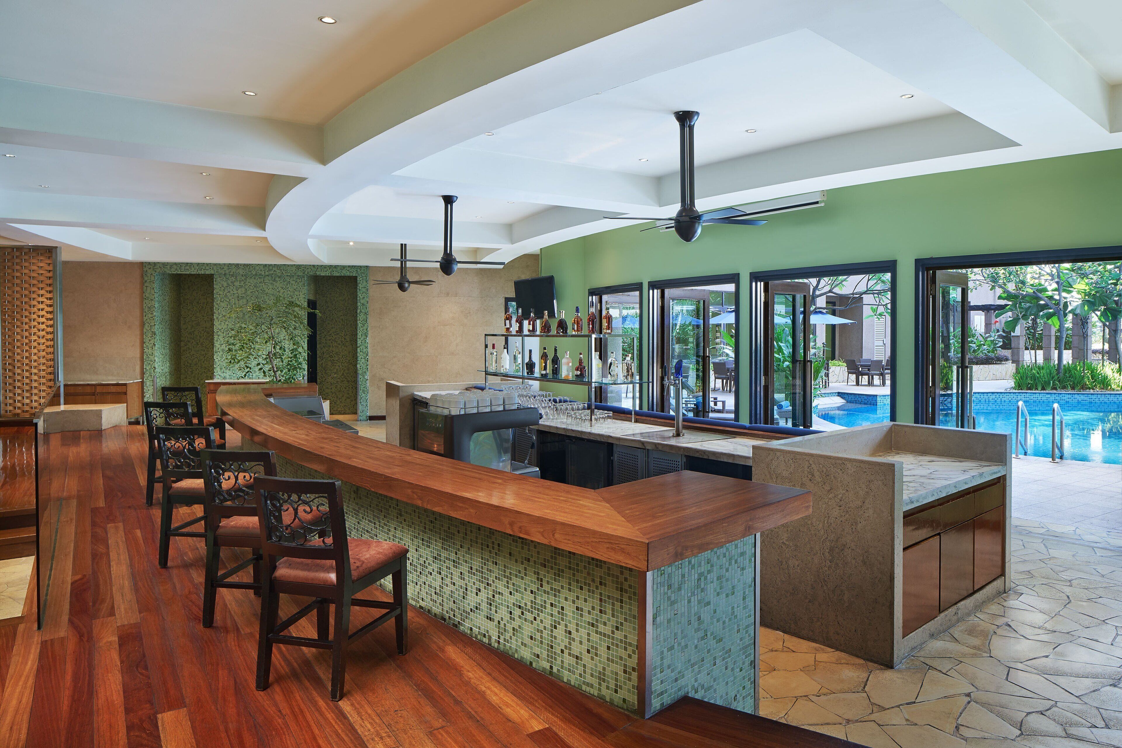 A bar area with a wooden counter, bar stools, and a pool view.