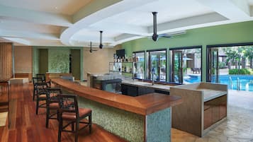 A bar area with a wooden counter, bar stools, and a pool view.