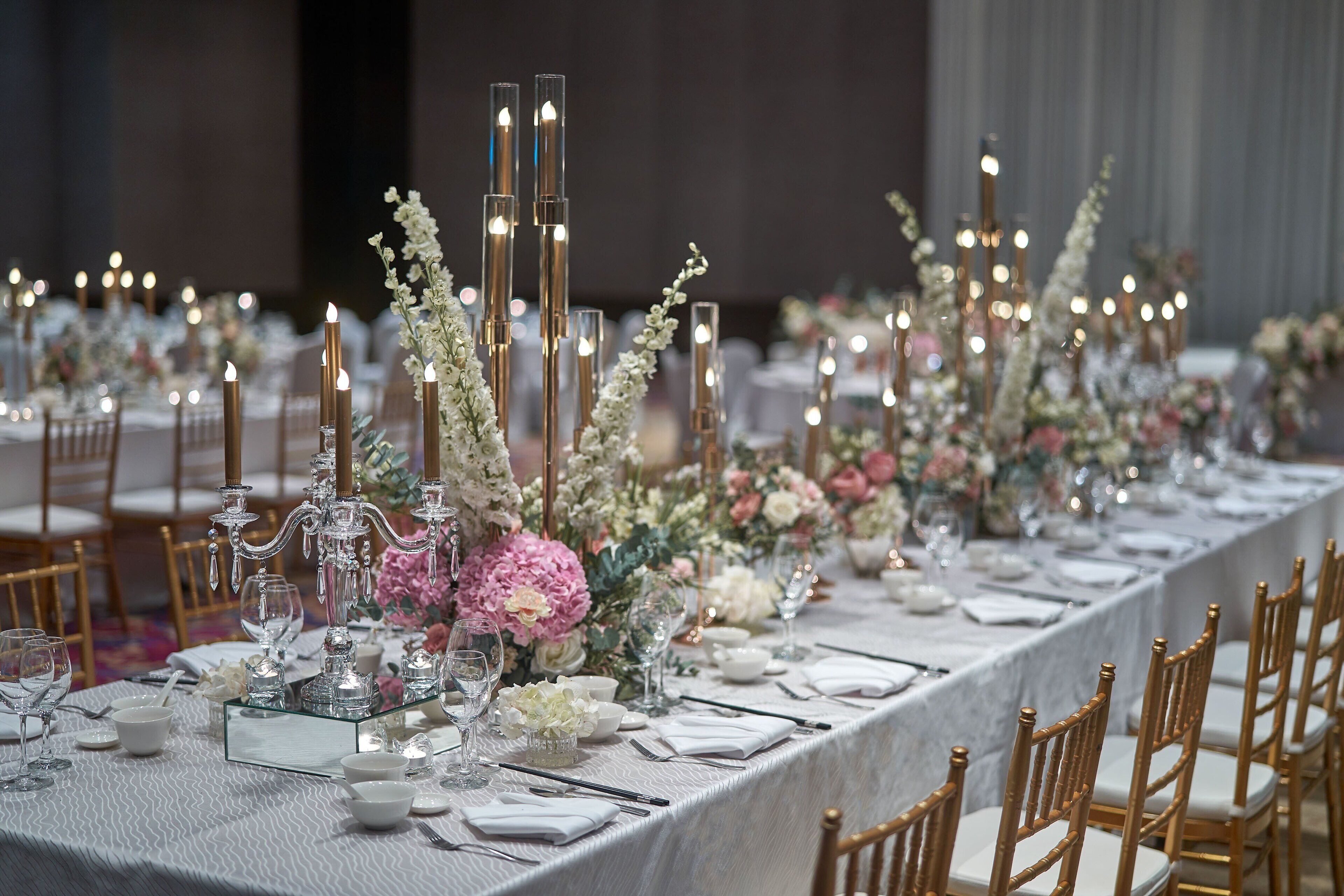 A long banquet table set with white tablecloths, gold chairs, and floral centerpieces.