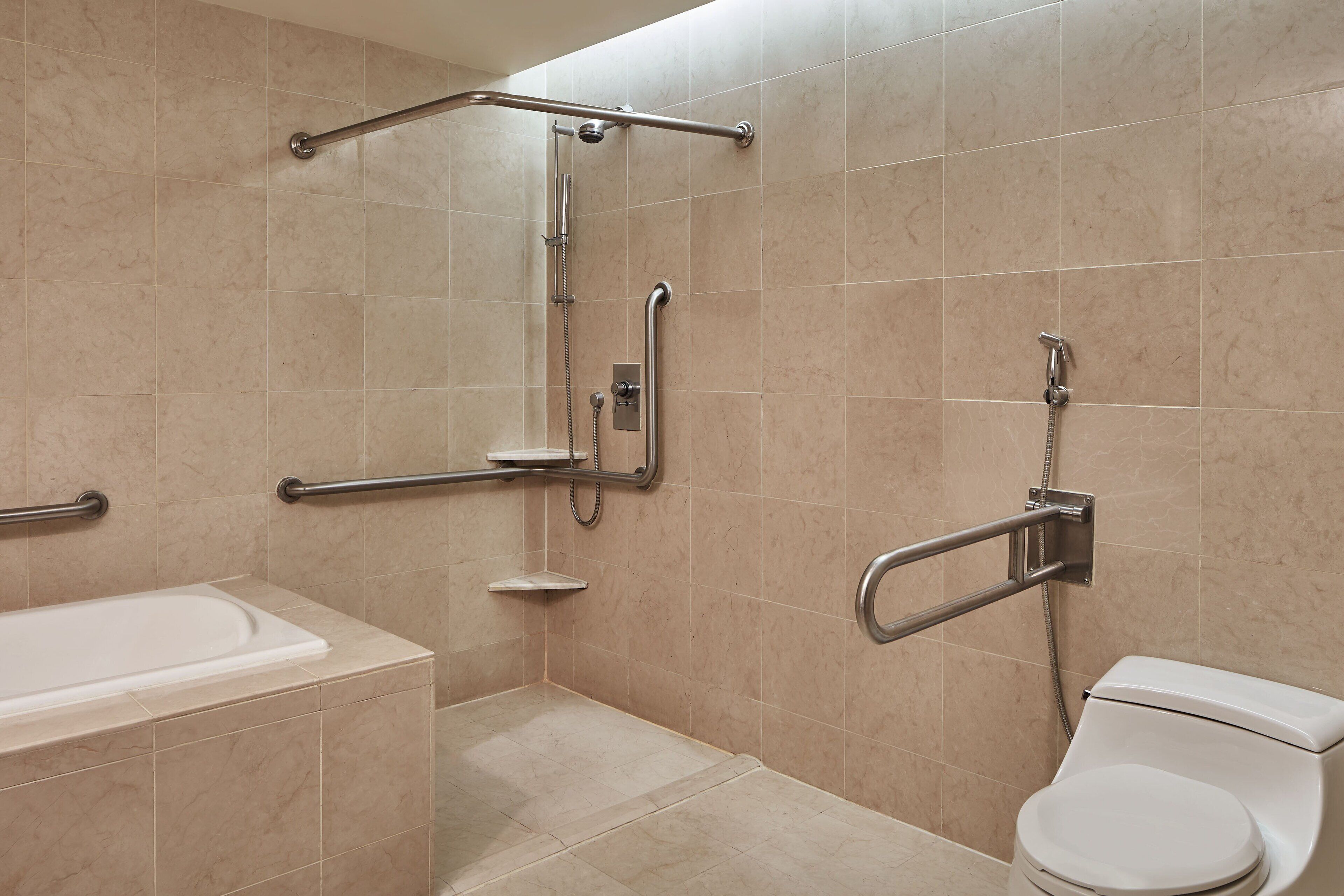 Une salle de bain équipée d’une baignoire, d’une douche avec des barres d’appui et de toilettes avec une barre d’appui de sécurité.