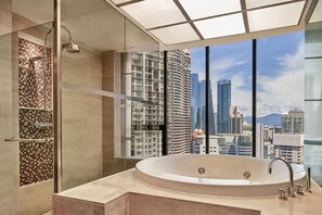 A modern bathroom with a large bathtub, a shower area, and a city view through large windows.