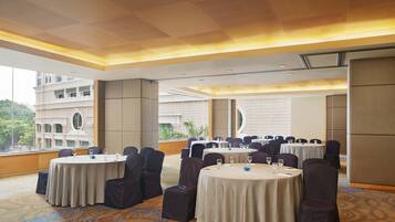 A conference room with round tables, dark chairs, and a large window offering a view of a building and greenery.