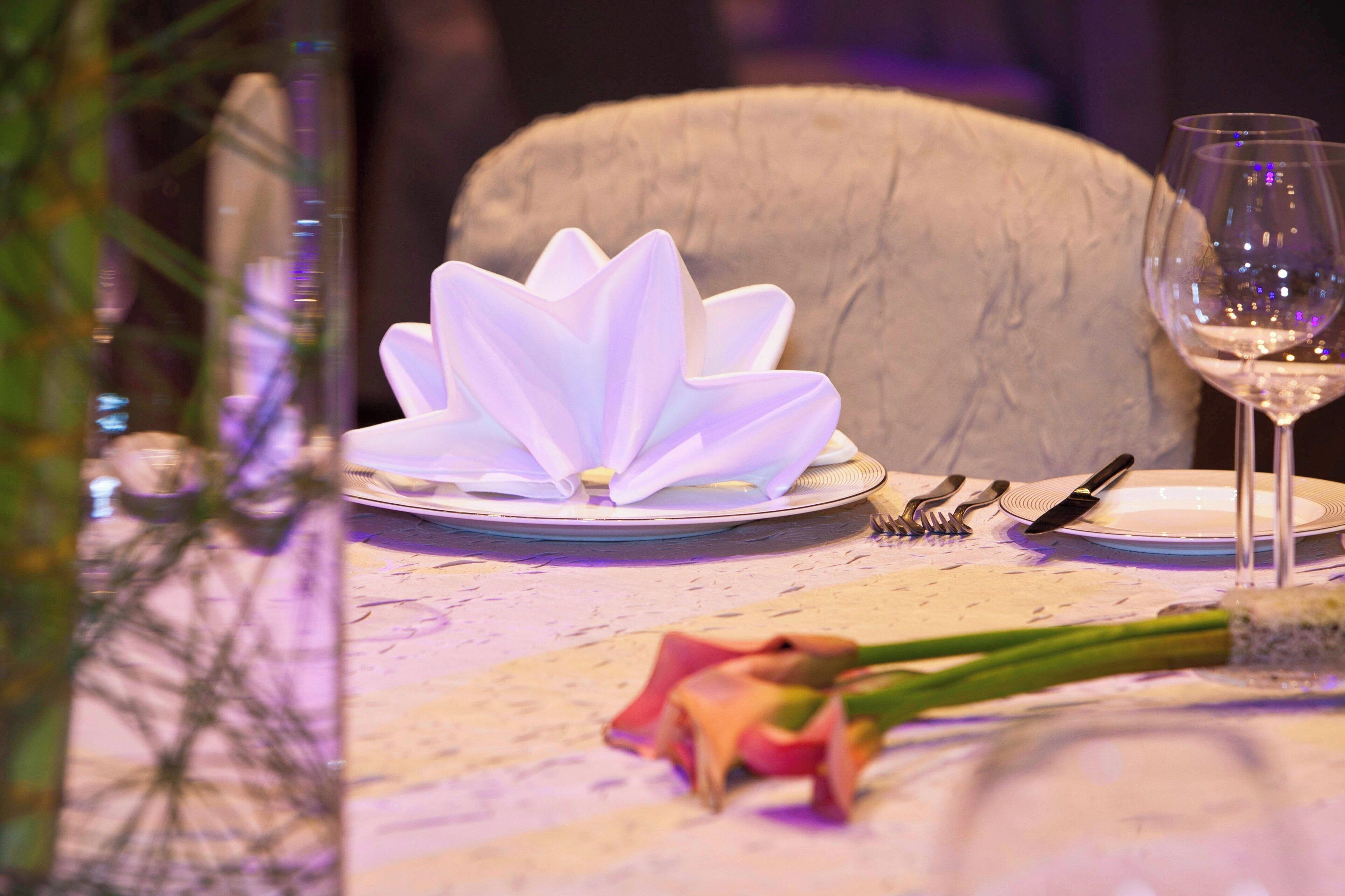 Une table dressée avec un arrangement floral blanc au centre, un verre à vin et une rose posée sur une nappe.