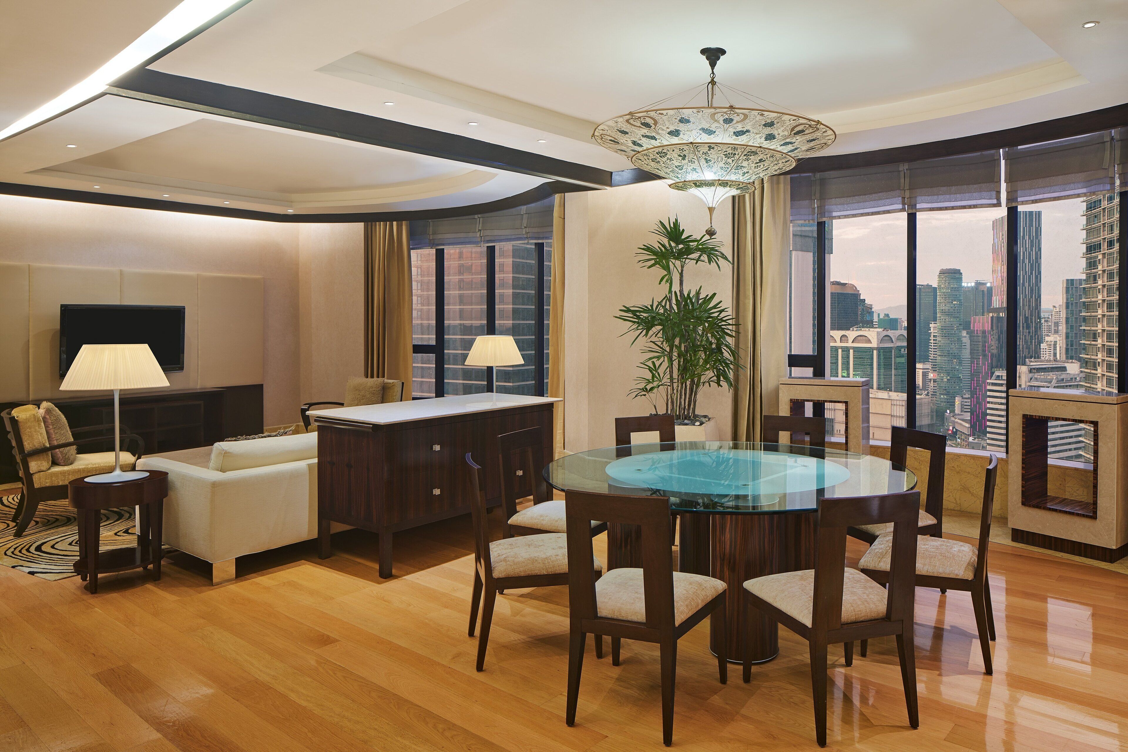 A modern living room with a glass dining table, wooden chairs, a sofa, and a TV.