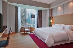 Habitación de hotel moderna con una cama grande, un escritorio con silla, televisión y vistas a la ciudad a través de amplios ventanales.