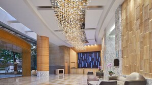 A spacious lobby with a high ceiling, a reception desk, seating area, and a decorative light fixture.