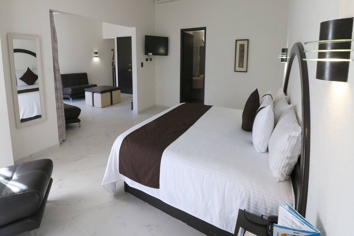 A modern hotel room with a large bed, a sofa, a desk, and a television.