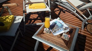 A deck with lounge chairs, a table with a magazine, a glass of orange juice, and a bottle of water, overlooking a beach. - Hotel Iruña (Mar del Plata)
