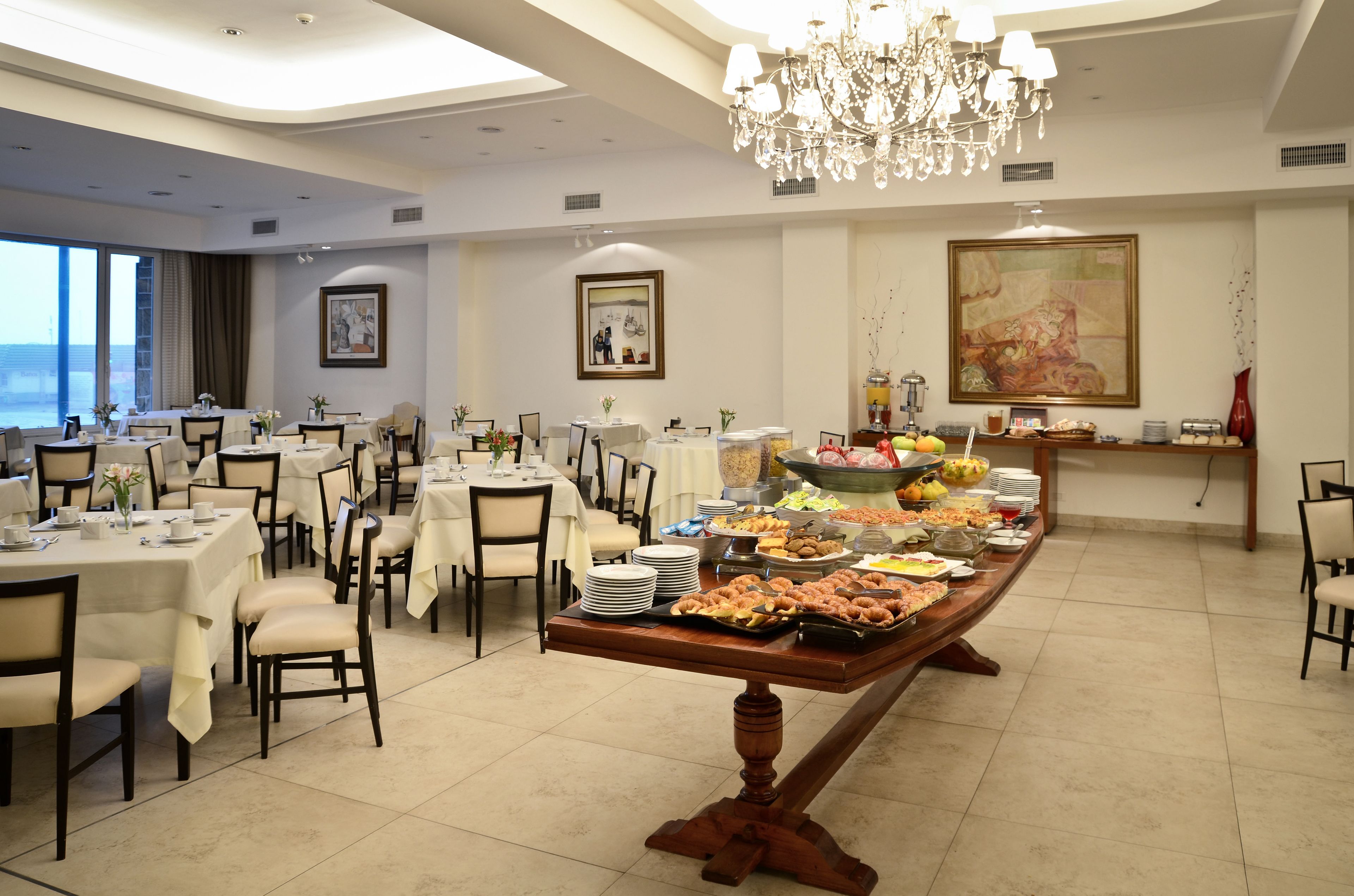 Un espace repas avec plusieurs tables, un buffet proposant divers plats et un lustre.