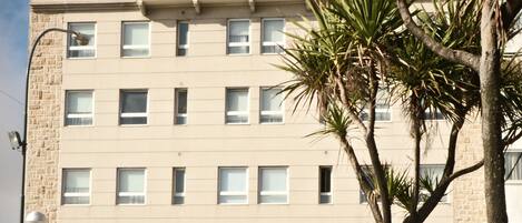 A hotel building with multiple windows and balconies, surrounded by a garden with various flowers.