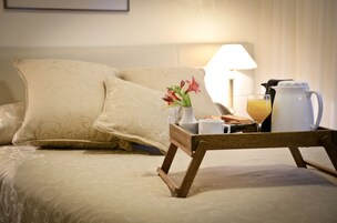 Una cama bien hecha con una bandeja de desayuno que incluye una jarrilla, un vaso de zumo de naranja y un pequeño florero con flores.