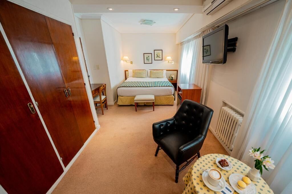 Une chambre d’hôtel avec un lit, une chaise, une table avec le petit-déjeuner et un téléviseur fixé au mur.
