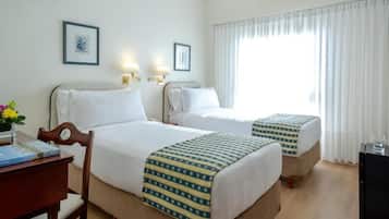 A hotel room with two beds, a desk, a chair, a lamp, and a window with curtains.