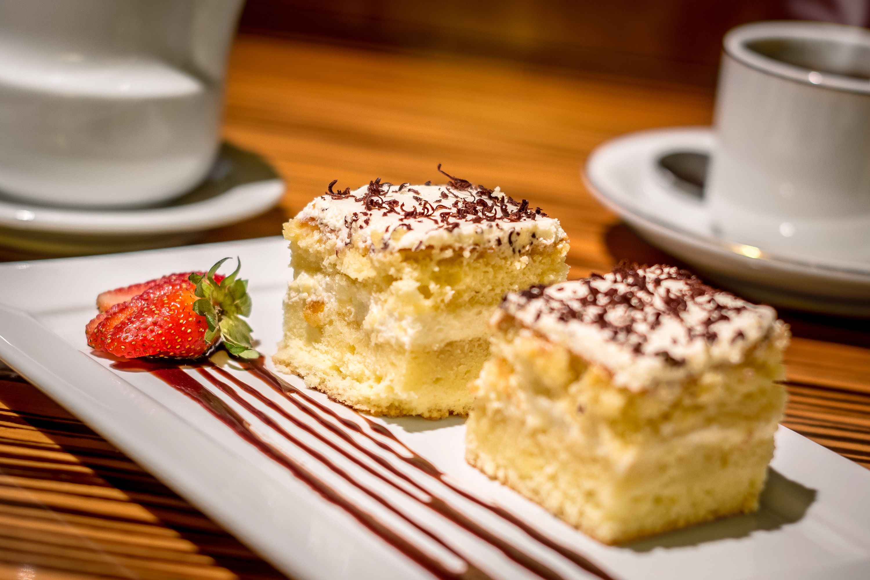 A dessert plate with two pieces of cake and a strawberry on a rectangular white plate.