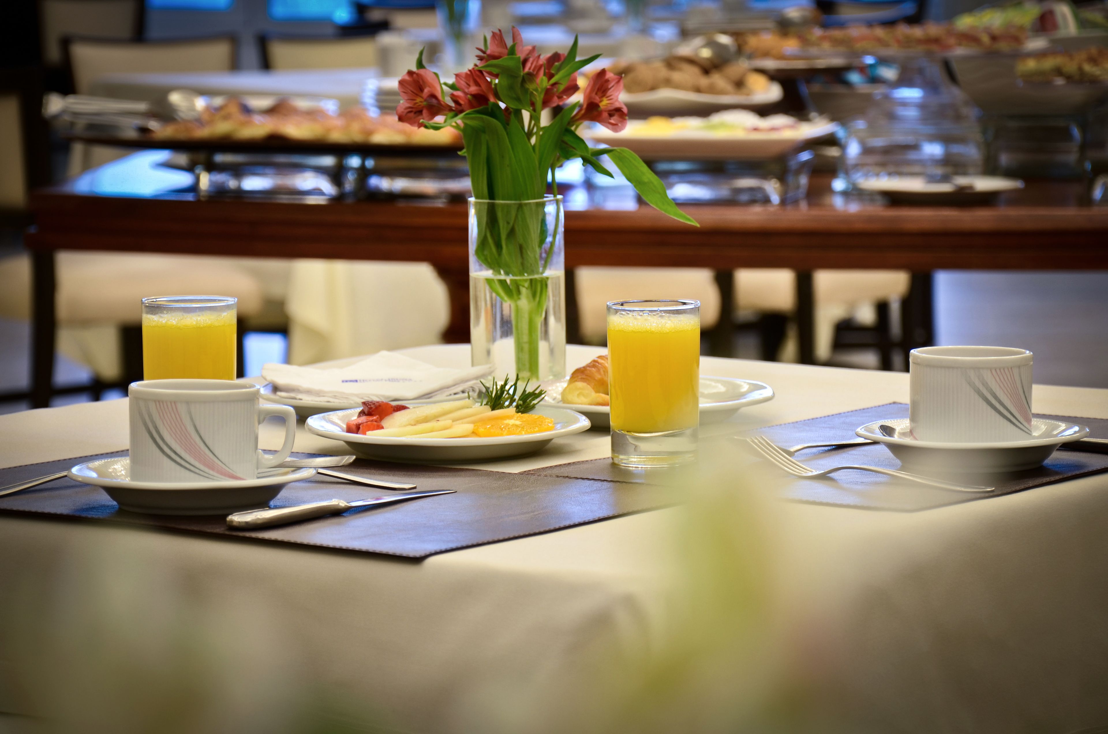 A breakfast setting with a table set for two, including plates of food, glasses of orange juice, and a vase with flowers.
