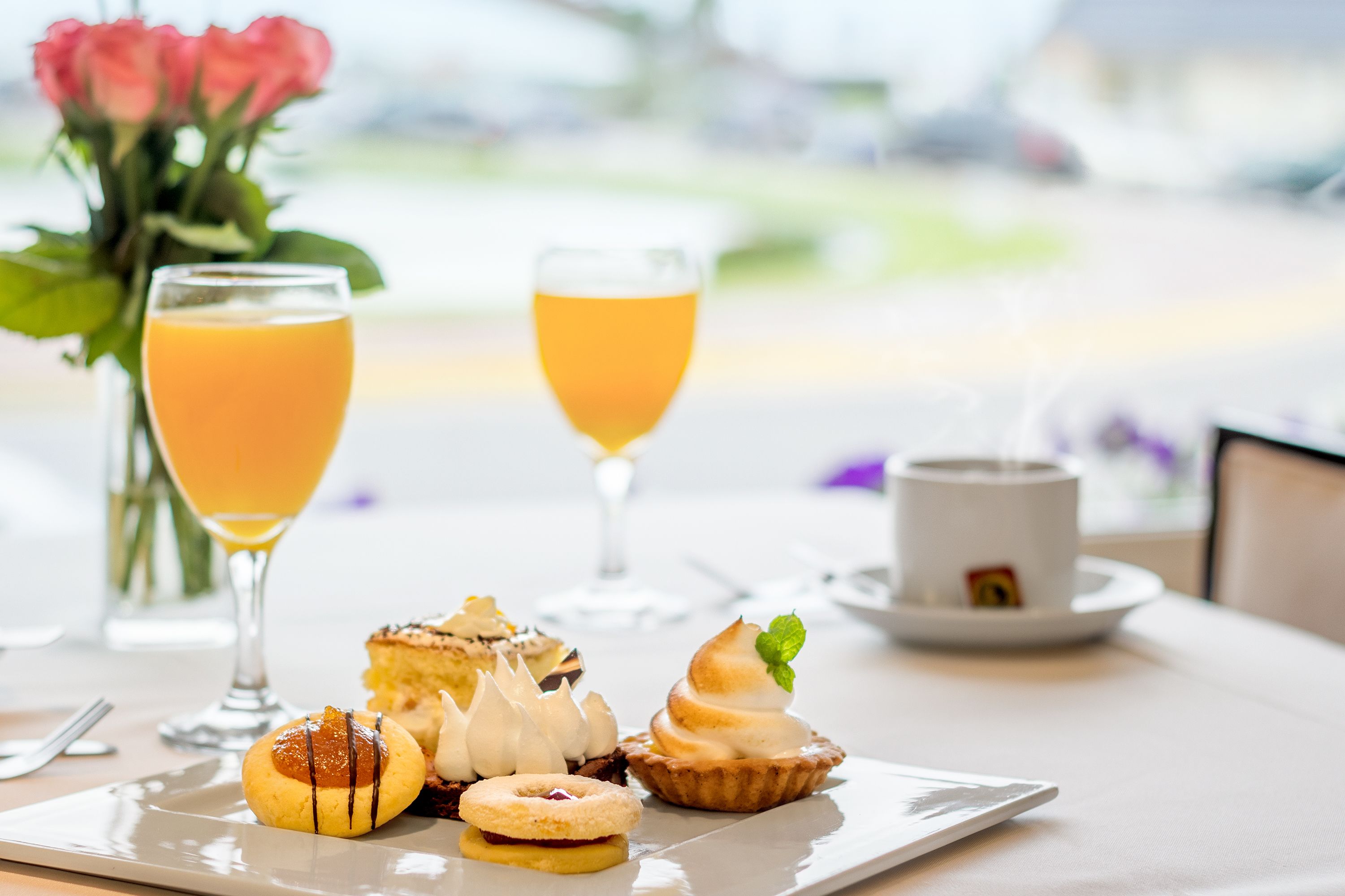 A breakfast setting with a plate of pastries, two glasses of orange juice, a cup of coffee, and a vase of flowers.