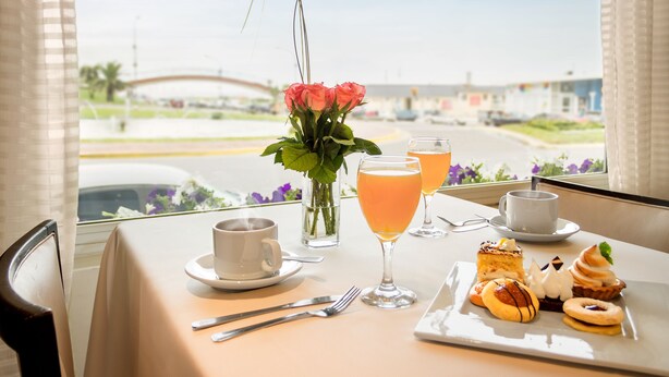 A breakfast table with a cup, a glass of orange juice, a plate of pastries, and a vase with flowers. - Hotel Iruña (Mar del Plata)