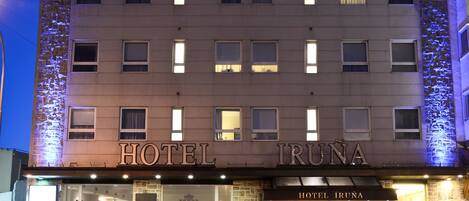 Ein Hotel mit einer Stein-Fassade, beleuchteten Fenstern und einem Schild mit der Aufschrift "HOTEL IRUNA".