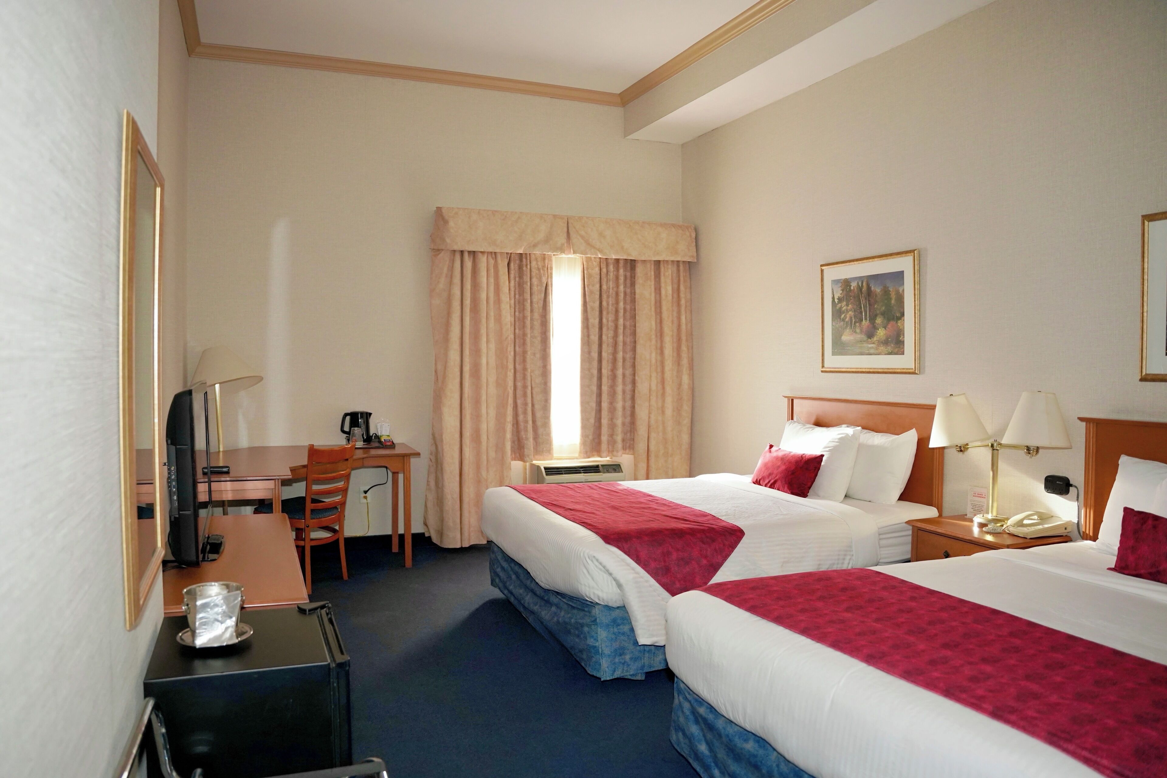 Habitación de hotel con dos camas, un escritorio, una silla, un televisor y una ventana con cortinas.