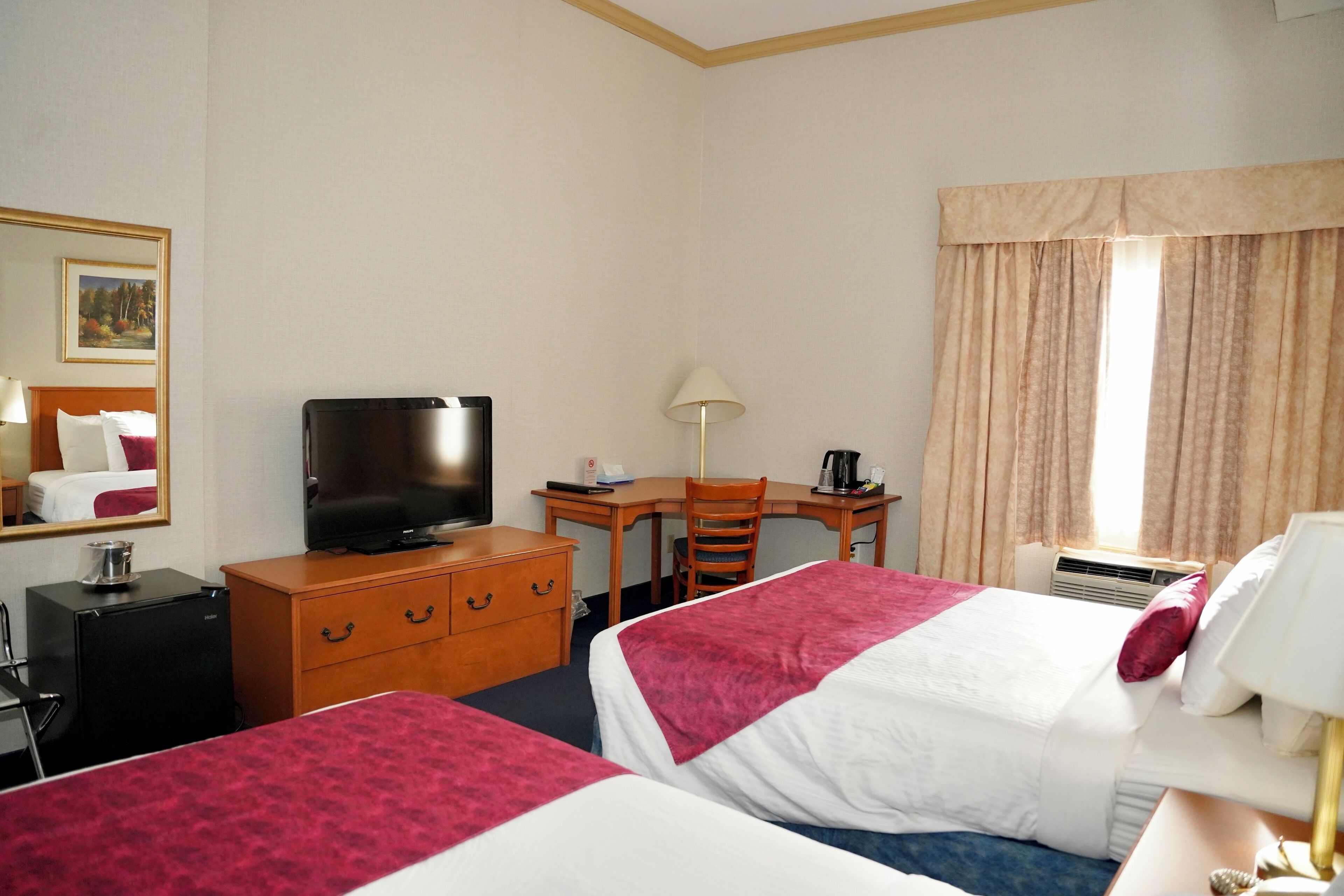 A hotel room with two beds, a desk, a television, a dresser, and a window with curtains.