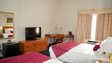 A hotel room with two beds, a desk, a television, a dresser, and a window with curtains.