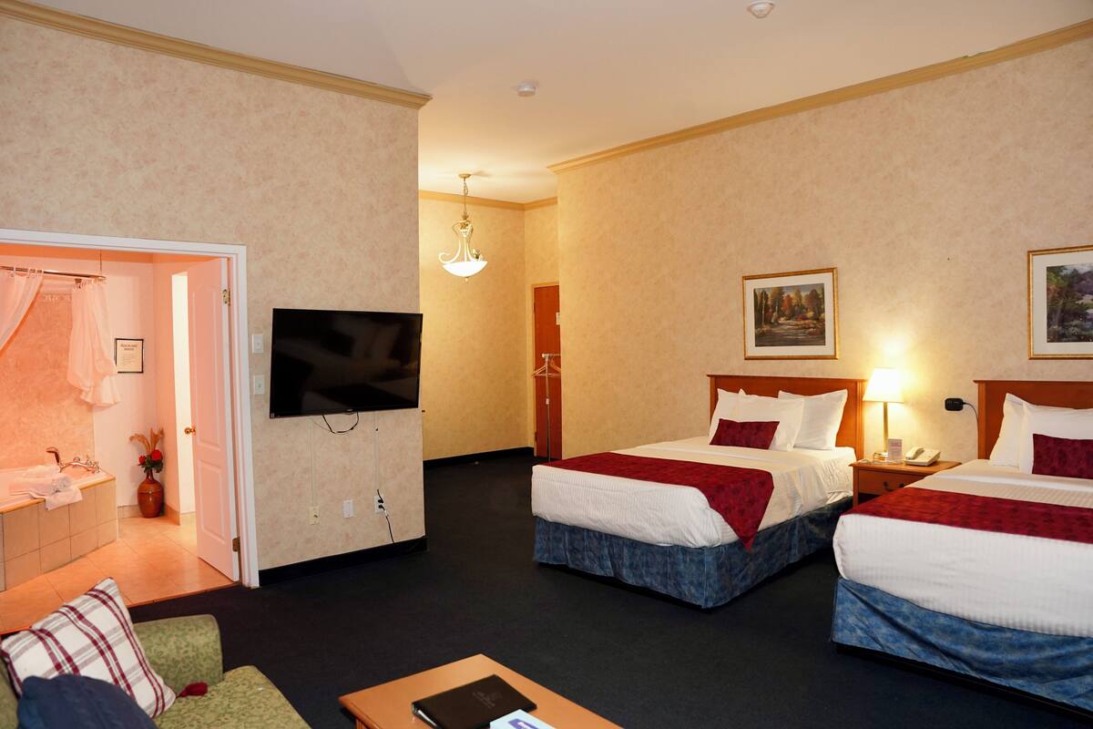 A hotel room with two beds, a TV, a desk, and a bathroom.