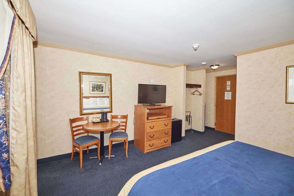 A hotel room with a bed, a desk with a chair, a television, a dresser, and a door.