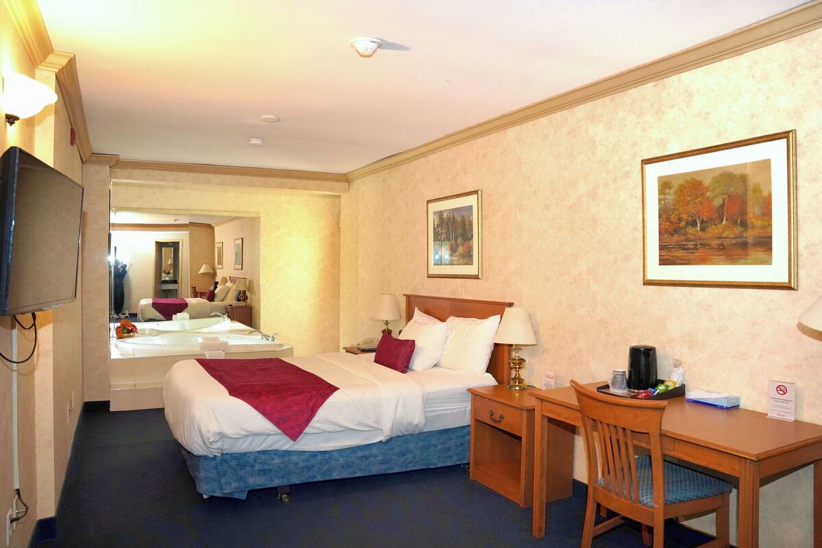 A hotel room with a bed, bedside table, chair, desk, and a television.