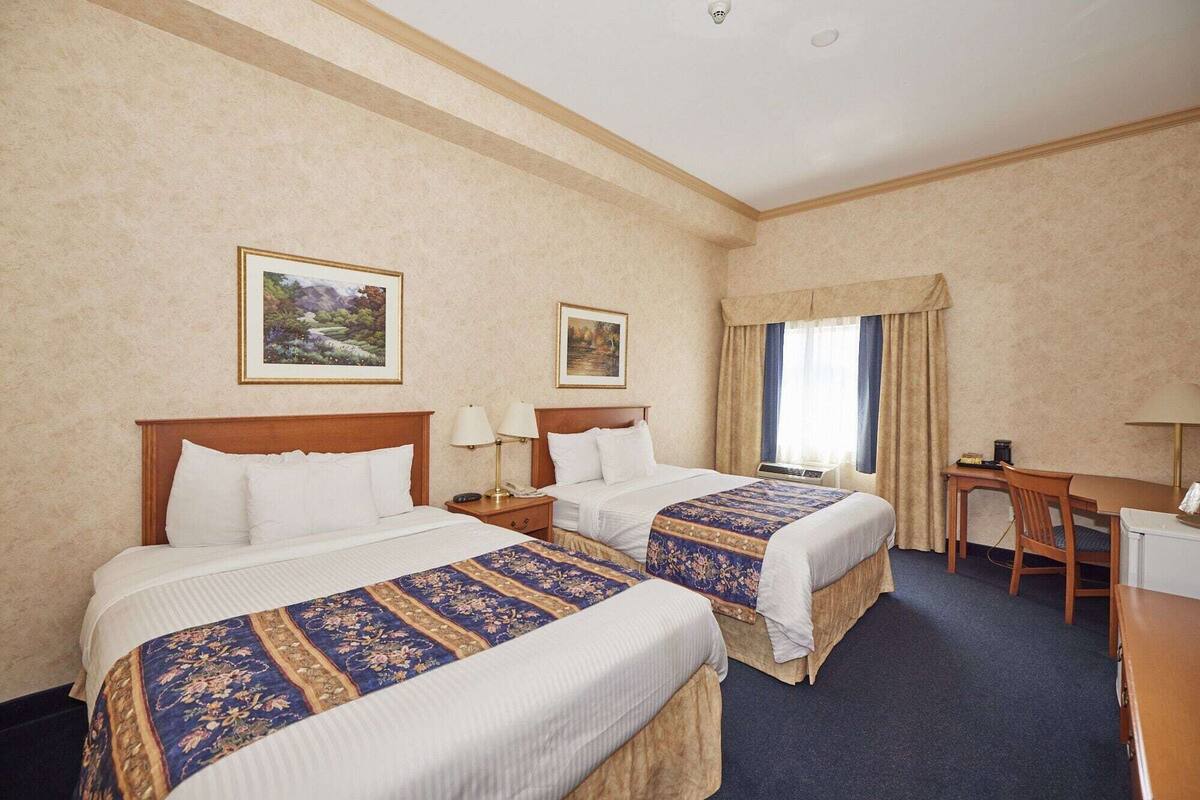 A hotel room with two beds, a desk, a chair, and a window with curtains.