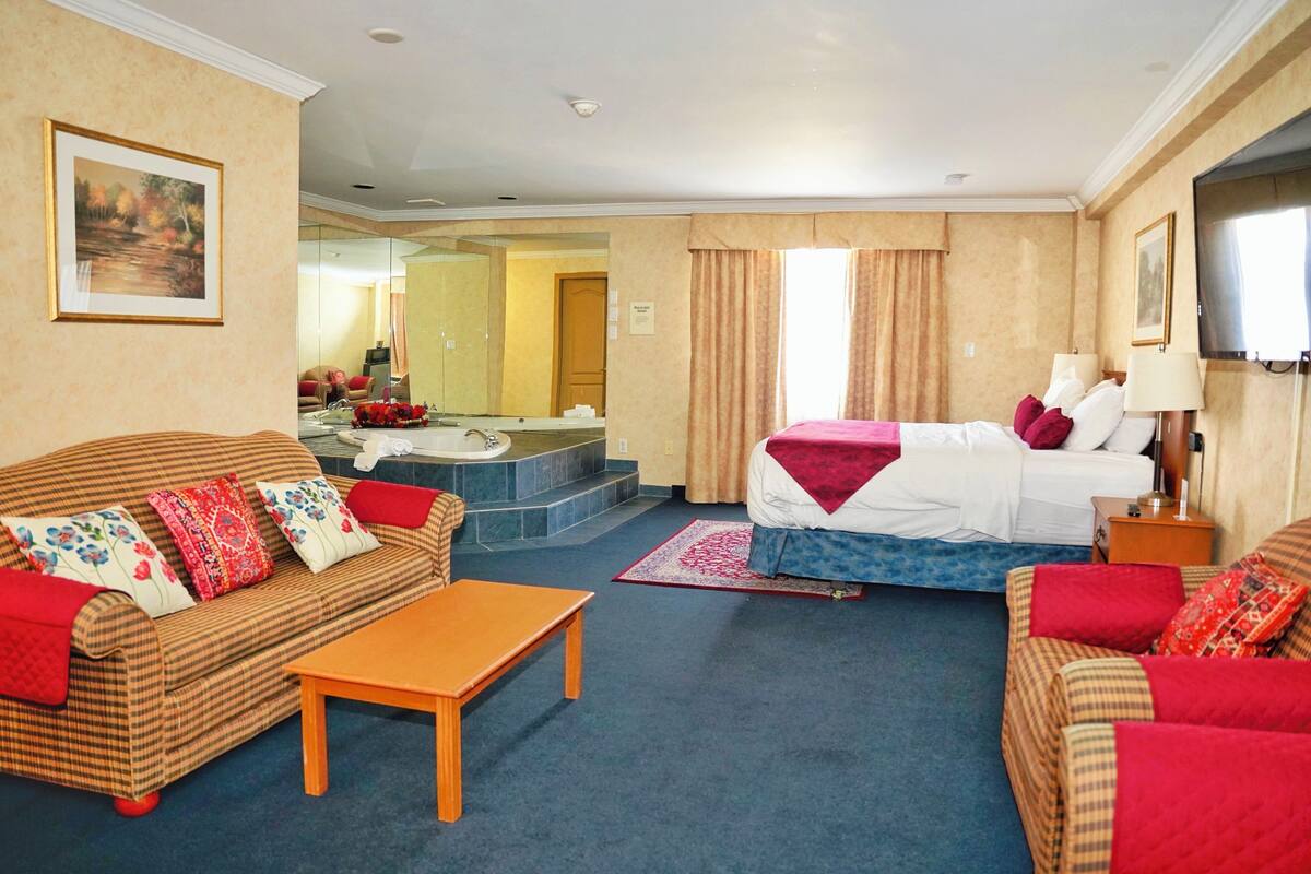 A hotel room with a bed, two sofas, a small table, a mirror, and a TV.