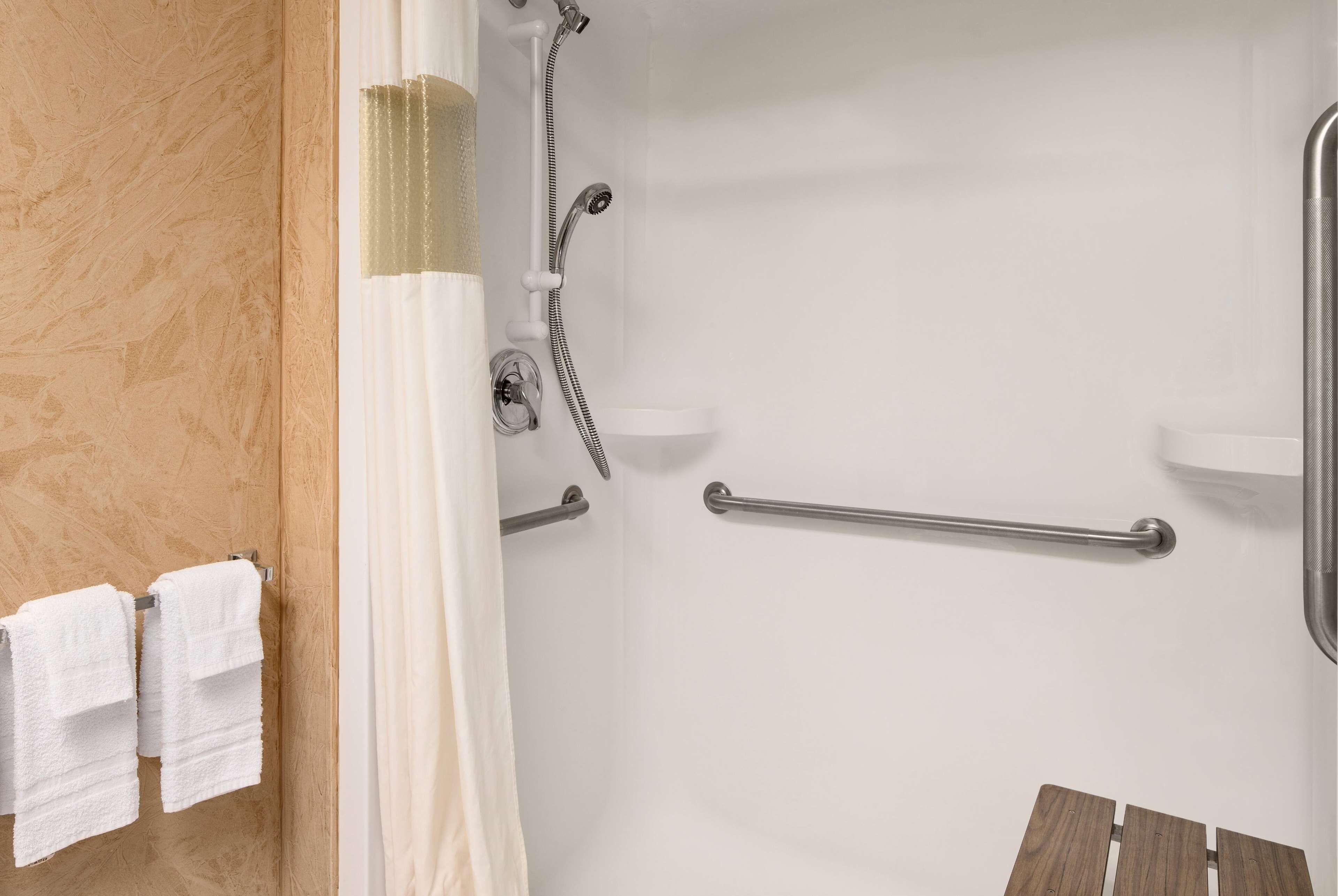 Un espace douche doté d’une porte en verre, d’un porte-serviettes avec des serviettes blanches et d’un banc en bois.