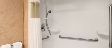 Un espace douche doté d’une porte en verre, d’un porte-serviettes avec des serviettes blanches et d’un banc en bois.