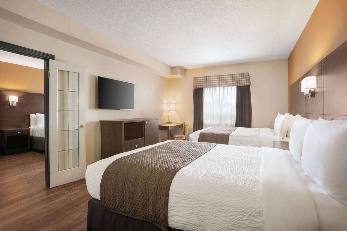 Une chambre d’hôtel avec deux lits, un bureau, une télévision et une fenêtre avec des rideaux.