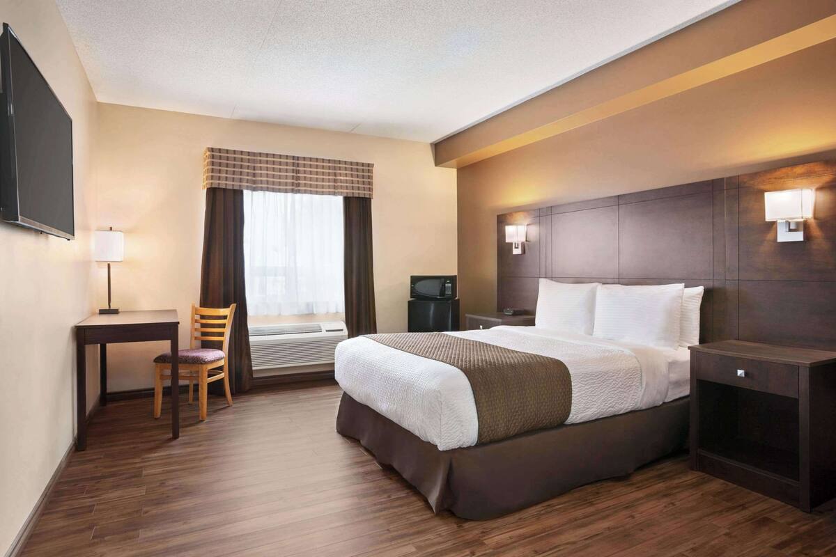 Une chambre d’hôtel avec un lit, un bureau, une chaise, une télévision et une fenêtre avec des rideaux.
