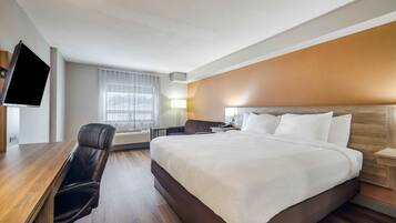 A hotel room with a bed, a desk, a chair, a TV, and a window with curtains.
