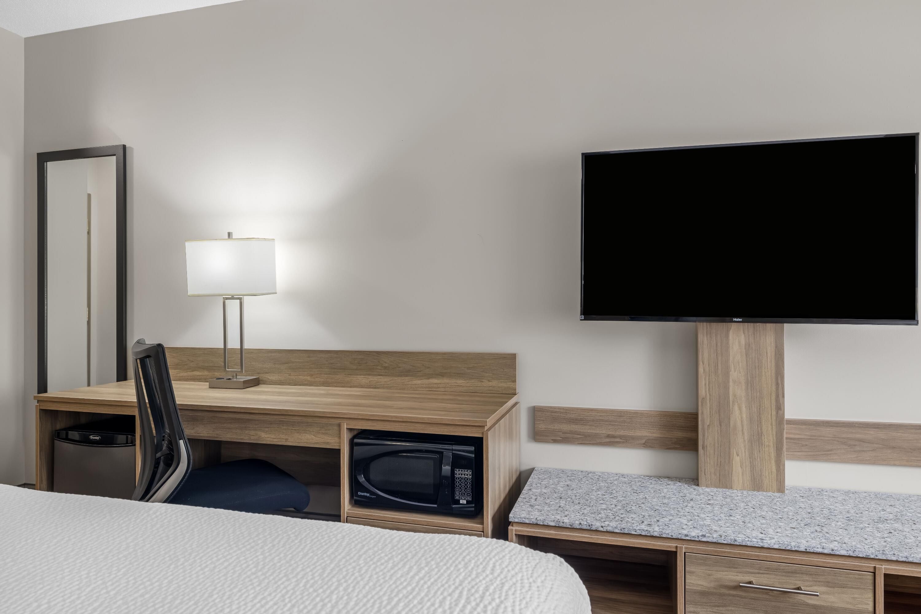 Una habitación de hotel con una cama, un escritorio con lámpara, televisión y microondas.
