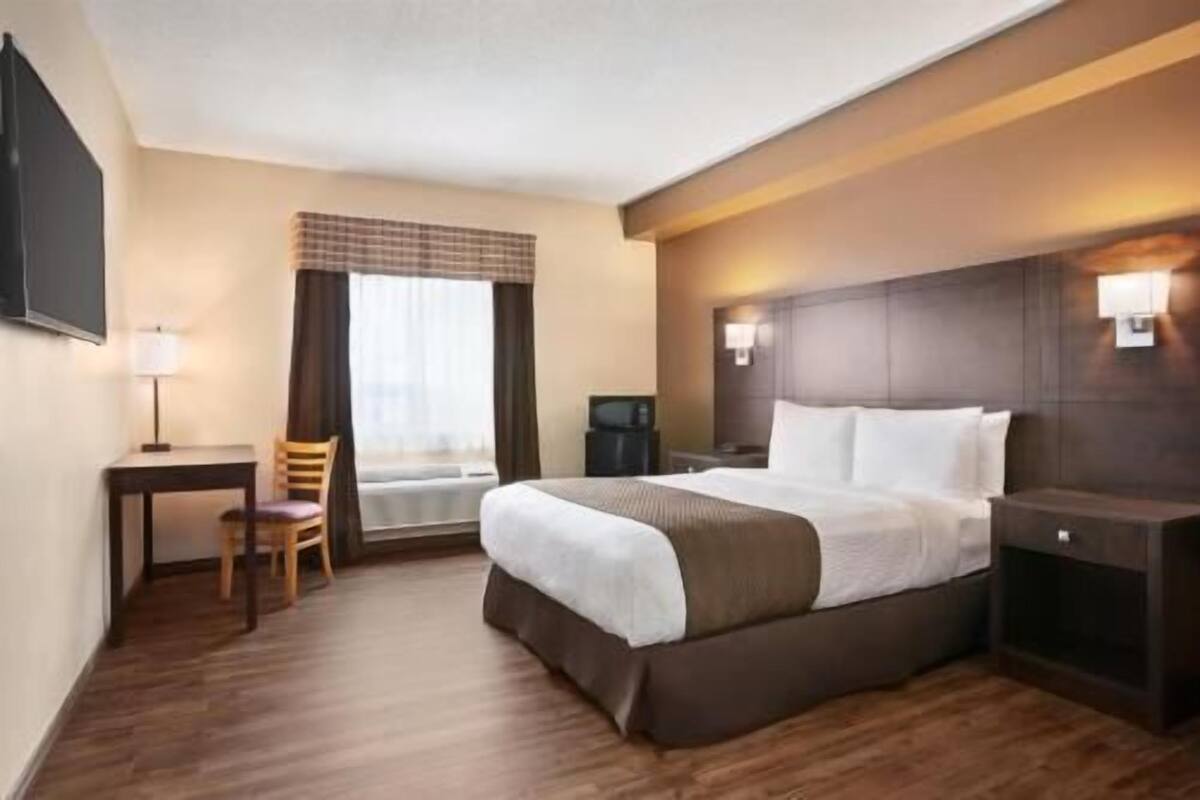 Une chambre d’hôtel équipée d’un lit, d’un bureau, d’une chaise, d’une télévision et d’une fenêtre avec des rideaux.