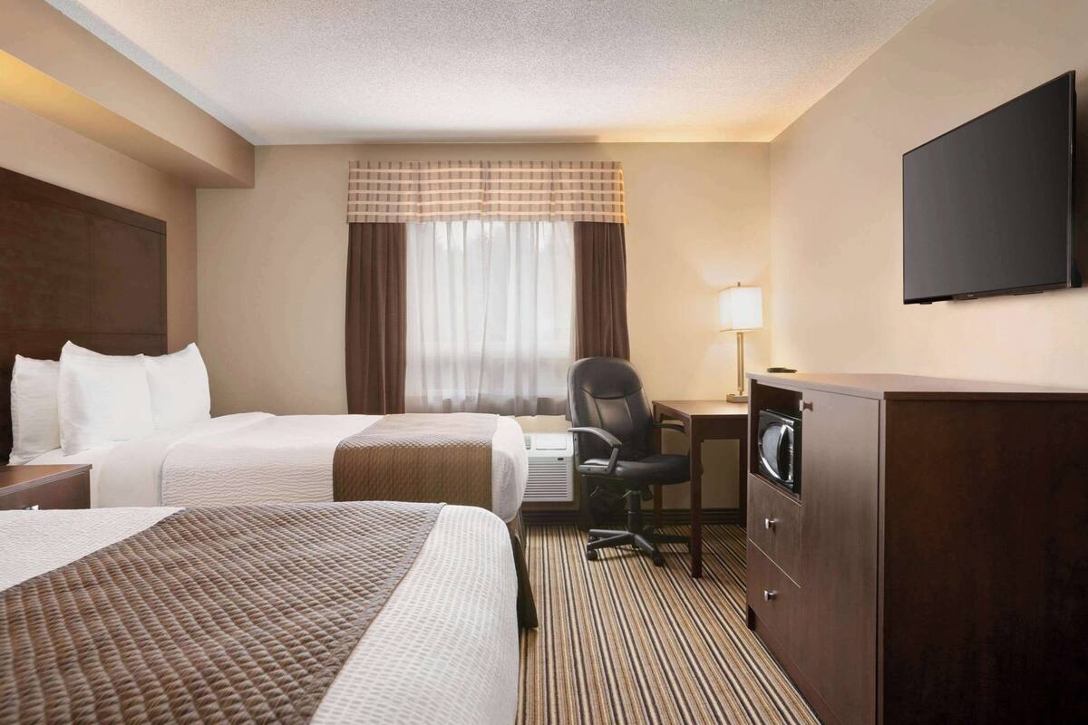 Une chambre d’hôtel avec deux lits, un bureau avec un ordinateur, une télévision et une armoire.