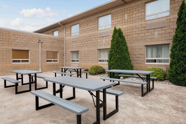 A courtyard with picnic tables, a brick building, and green bushes.