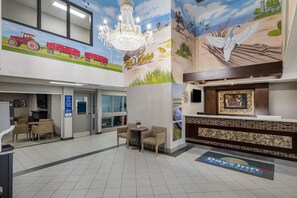 Un hall d’hôtel agrémenté d’un lustre, d’un comptoir d’accueil et d’une fresque représentant des oiseaux.