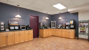 A commercial kitchen with wooden cabinets, a marble-tiled floor, and various appliances like a coffee machine and a microwave. - Days Inn by Wyndham Leamington (Leamington)