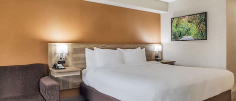 Una habitación de hotel con una cama, un escritorio con teléfono, una silla y un cuadro en la pared.