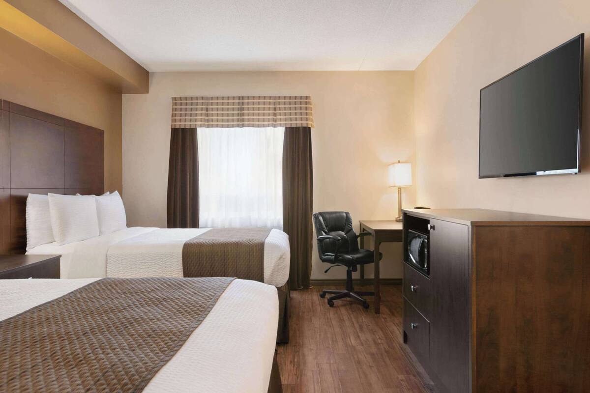 Une chambre d’hôtel avec deux lits, un bureau avec une chaise, une télévision et un placard.