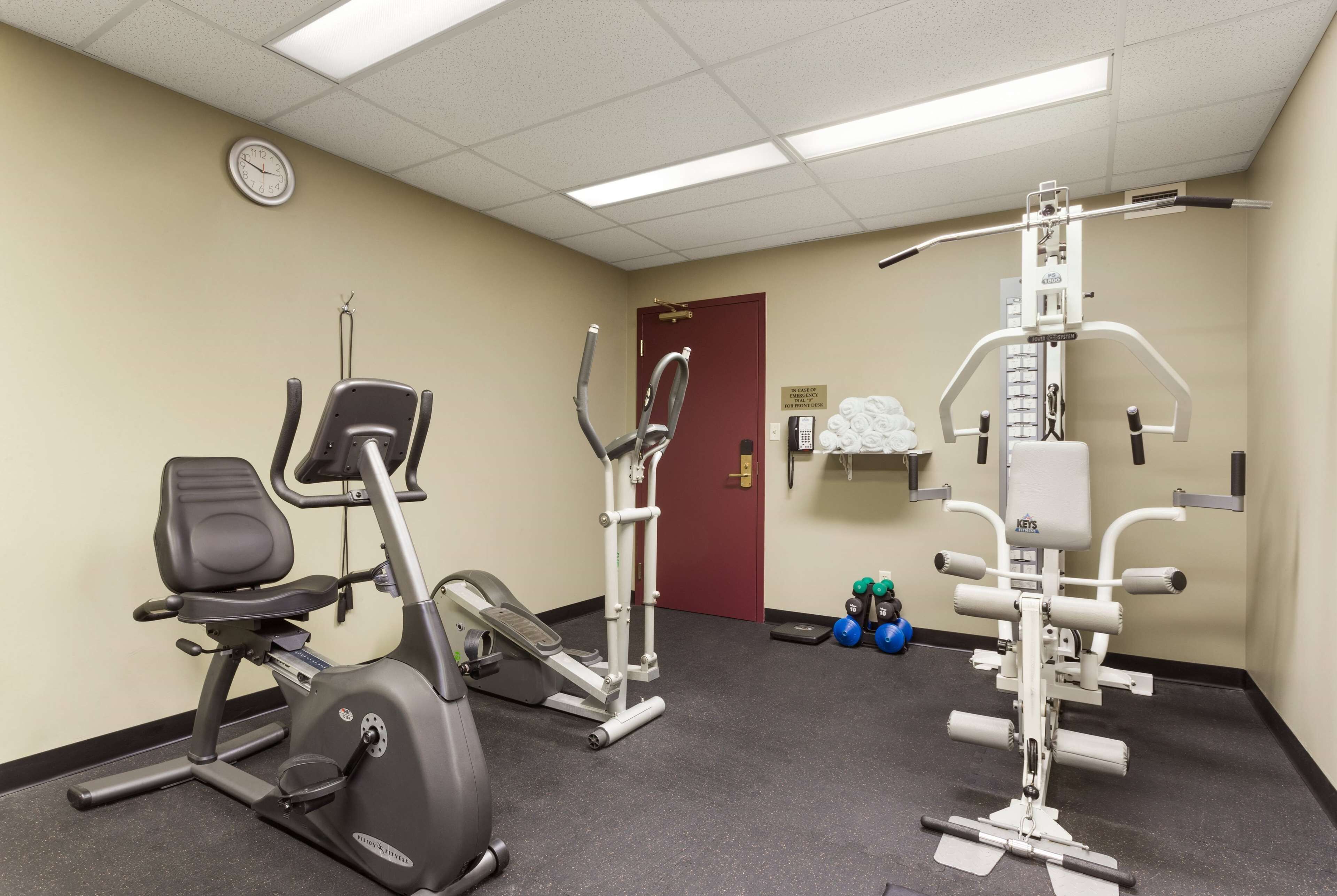Une salle de sport équipée de matériel d’exercice, une horloge au mur et une porte à l’arrière-plan.