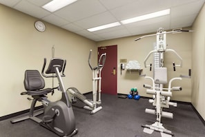 A fitness room with exercise equipment, a clock on the wall, and a door in the background.