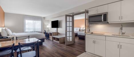 Ein Hotelzimmer mit einem Bett, einem Schreibtisch mit Stuhl, einem Fernseher, einer Mikrowelle und einer Küchenzeile.
