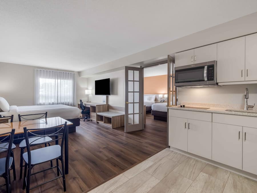 A hotel room with a bed, a desk with a chair, a TV, a microwave, and a kitchenette.
