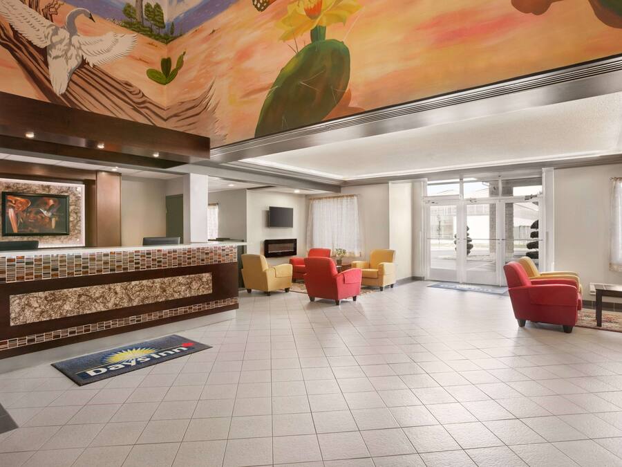 Et hotellobby med reception, siddeområde og et muralmaleri i loftet.